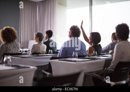 Medium group of conference participants sitting in conference room with woman raising hand Stock Photo