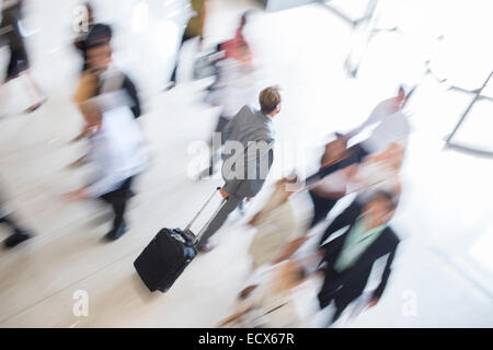 Businessman walking through lobby of public building towards exit, wheeling trolley case Stock Photo