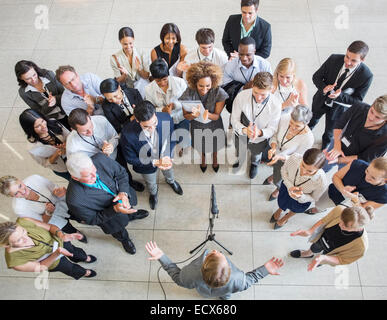 Applauding audience standing before man talking into microphone in lobby of conference center Stock Photo