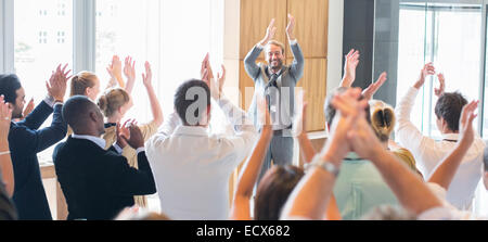 Portrait of smiling man standing before audience in conference room, applauding Stock Photo