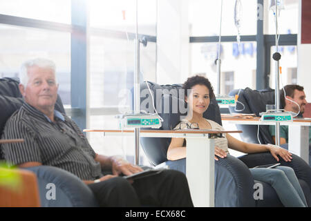 Patients sitting in armchairs receiving medical treatment in hospital ward Stock Photo