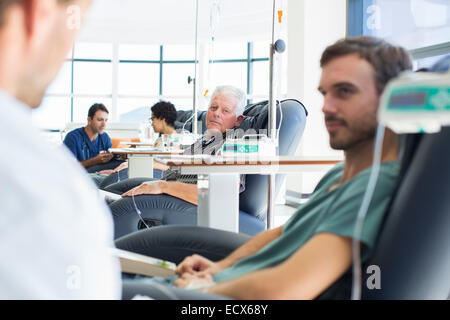 Doctors talking to patients receiving medical treatment in hospital ward Stock Photo