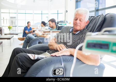 Senior patient receiving medical treatment sitting and looking down in hospital ward Stock Photo