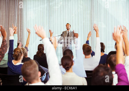 Businessman giving presentation in conference room, people raising hands Stock Photo