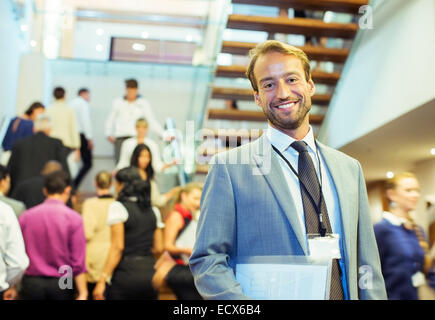 Portrait of smiling businessman holding file, standing in crowded lobby of conference center Stock Photo