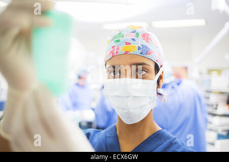 Masked surgeon adjusting saline bag during surgery Stock Photo