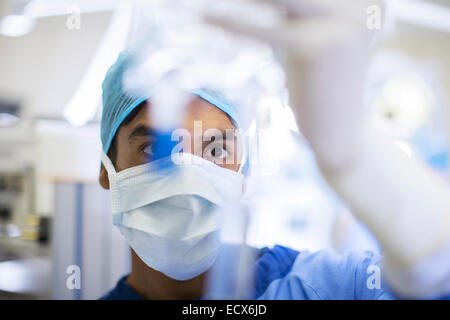 Surgeon wearing surgical mask, cap and gloves looking closely at IV drip Stock Photo