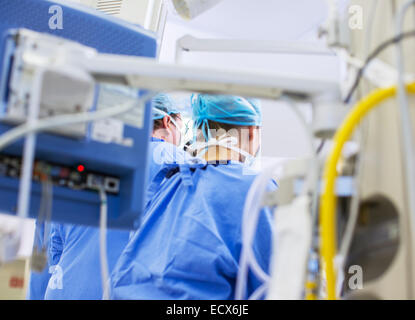 Rear view of doctors in operating theater, medical equipment in foreground Stock Photo