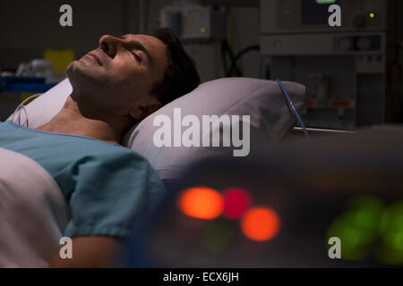 Patient lying in hospital bed in intensive care unit, medical equipment in foreground Stock Photo
