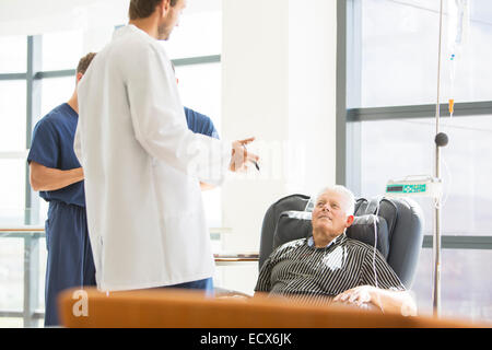 Two doctors talking to senior patient undergoing medical treatment in outpatient clinic Stock Photo