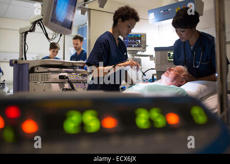 Doctors attending patient in intensive care unit, monitoring equipment in foreground Stock Photo