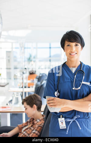 Portrait of doctor with arms crossed, patient undergoing medical treatment in background Stock Photo