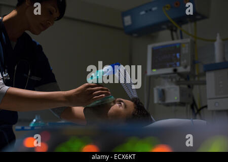 Doctor holding oxygen mask over patient's face in intensive care unit Stock Photo