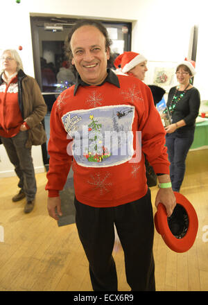 Huntington, New York, USA. 20th Dec, 2014. A smiling man wears a festive colorful Christmas sweater at the Jingle Boom Holiday Bash, which awarded prizes to people wearing the most creative or Ugly Sweaters, at the Main Street Gallery of Huntington Arts Council. Sparkboom, an HAC project, provides events such as this geared to Gen-Y, 18-34 years of age, to address the 'brain drain' of creative young professionals of Long Island. The paintings on the art gallery walls were the Annual Juried Still Life Show. Credit:  Ann Parry/ZUMA Wire/Alamy Live News Stock Photo