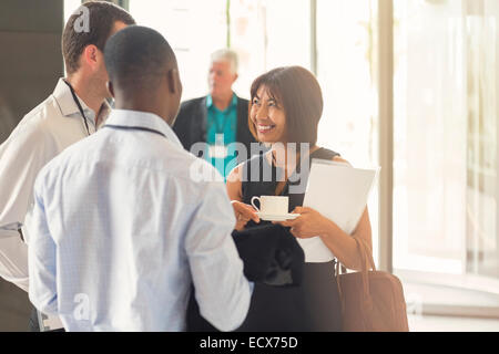 Businesswoman talking to colleagues holding coffee cup in office Stock Photo
