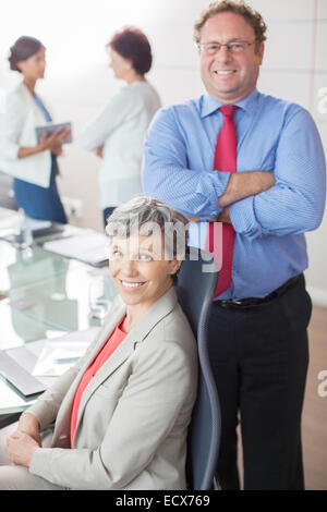 Two mature business people looking at camera, smiling in conference room Stock Photo