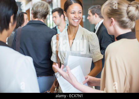 Portrait of two smiling women holding files and talking, standing in crowded lobby Stock Photo