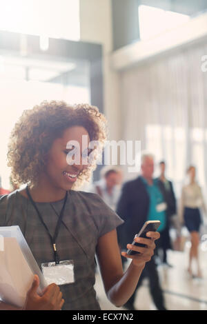 Portrait of smiling young woman standing in lobby of conference center, using smartphone Stock Photo