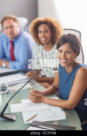 Beautiful woman sitting at conference table talking into microphone Stock Photo