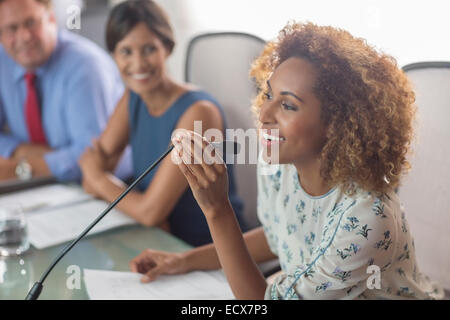 Beautiful woman sitting at conference table talking into microphone Stock Photo