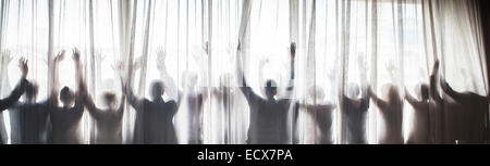 Silhouette of people raising hands behind transparent curtain Stock Photo