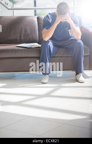 Portrait of young doctor with head in hands sitting on sofa Stock Photo