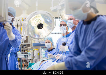 Doctors performing surgery in operating theater, looking at monitor Stock Photo