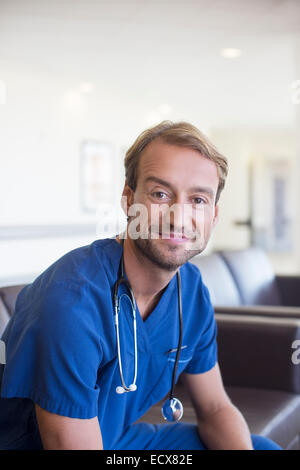 Portrait of mid adult doctor smiling and sitting on leather sofa in hospital corridor Stock Photo