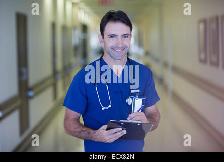 Portrait of male doctor holding clipboard in hospital corridor Stock Photo