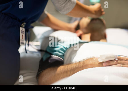 Doctor holding oxygen mask over male patient's mouth in intensive care unit Stock Photo