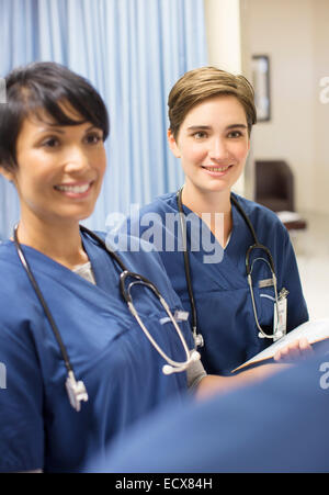 Two smiling doctors wearing scrubs with stethoscopes around necks in hospital Stock Photo