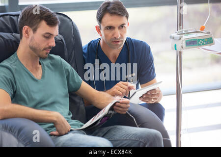 Doctor holding digital tablet, talking to patient undergoing medical treatment in hospital Stock Photo