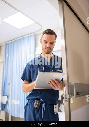 Male doctor standing in doorway, taking notes on clip board in hospital Stock Photo