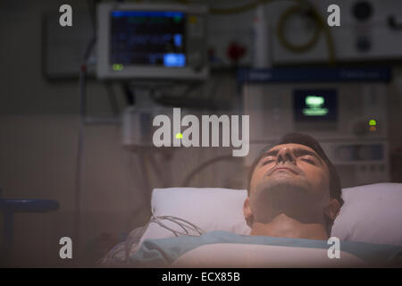 Patient lying in bed, surrounded by monitoring medical equipment in intensive care unit Stock Photo