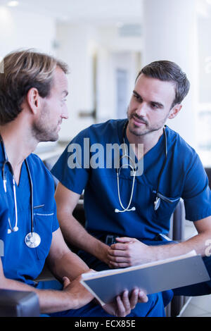 Two male doctors with stethoscopes, wearing scrubs talking in hospital Stock Photo