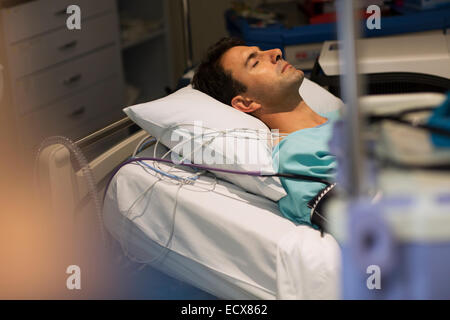 Patient attached to medical monitoring equipment lying in bed in intensive care unit Stock Photo