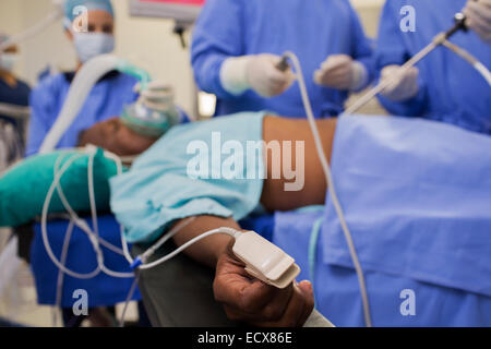 Doctors performing laparoscopic surgery, patient with pulse oxymeter on finger Stock Photo