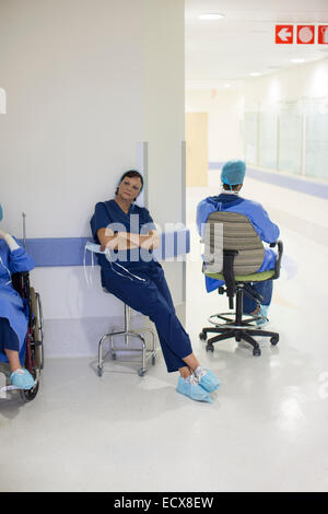 Two doctors wearing surgical clothing resting in hospital corridor Stock Photo