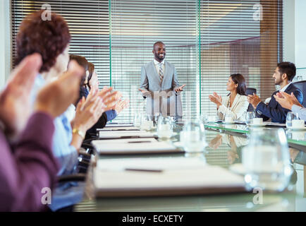 Businessman standing in conference room giving speech, colleagues clapping hands Stock Photo