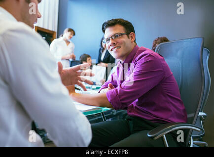 Businessmen talking during meeting in conference room with colleagues in background Stock Photo