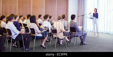 Young woman delivering speech before audience in conference room Stock Photo