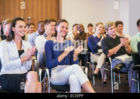 Portrait of two smiling women sitting in among other conference participants in conference room, applauding Stock Photo