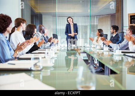 Conference participants applauding to young businesswoman standing at head of conference table Stock Photo