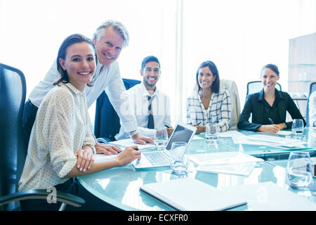 Three businesswomen and two businessmen sitting at conference table, smiling Stock Photo