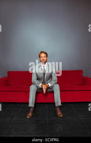 Portrait of businessman wearing grey suit sitting with hands clasped in dark room Stock Photo