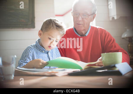 Boy reading with grandfather at table Stock Photo