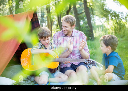 Father and sons playing guitar near camping tent Stock Photo