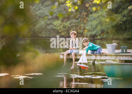 Boys fishing and playing with toy sailboat at lake Stock Photo