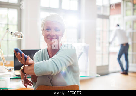 Businesswoman using cell phone at home office desk Stock Photo