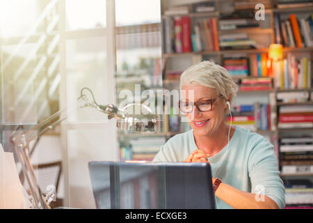 Businesswoman listening to earbuds and working in home office Stock Photo